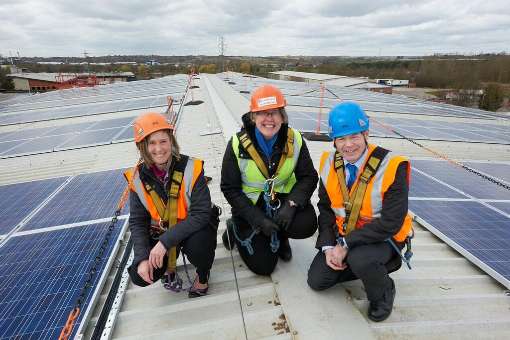 three trades people in high vis and hard hats, kneeling on a roof, with solar panels, showing Blue Patch's commitment to sustainable investments and fighting climate change.