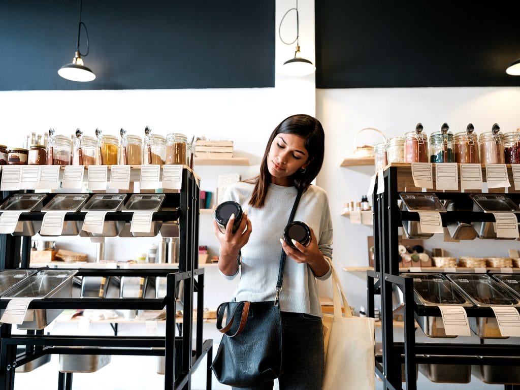 woman in a shop, looking at two products, making a selection as to which is the most ethical