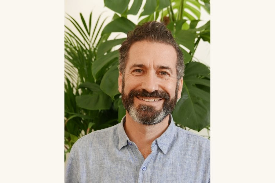 Smiling man with a beard and house plants behind him.