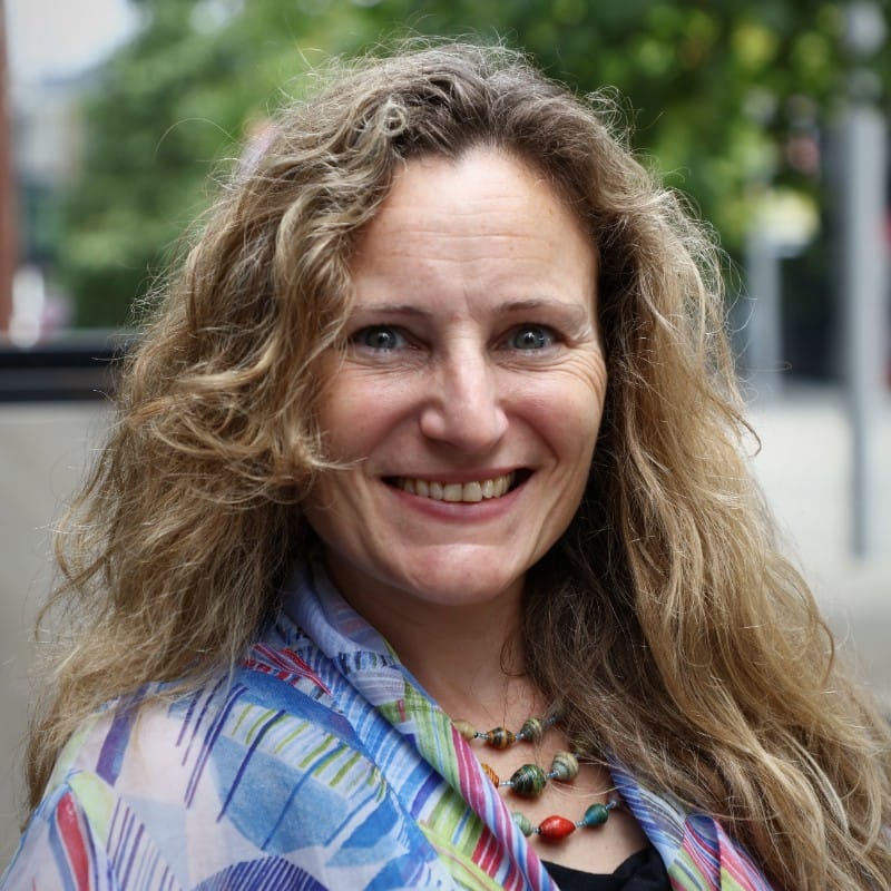 Smiling woman with curly, long hair, wearing a blue scarf, Liberty will be explaining Net Zero and carbon calculation