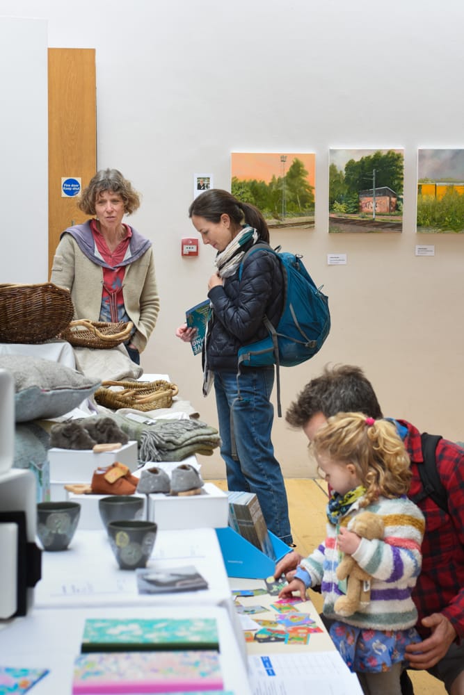 Angela Cole in the Linbury Room shows baskets to visitors at Blue patch's Sustainable Arts & Crafts Showcase at Dulwich Picture Gallery