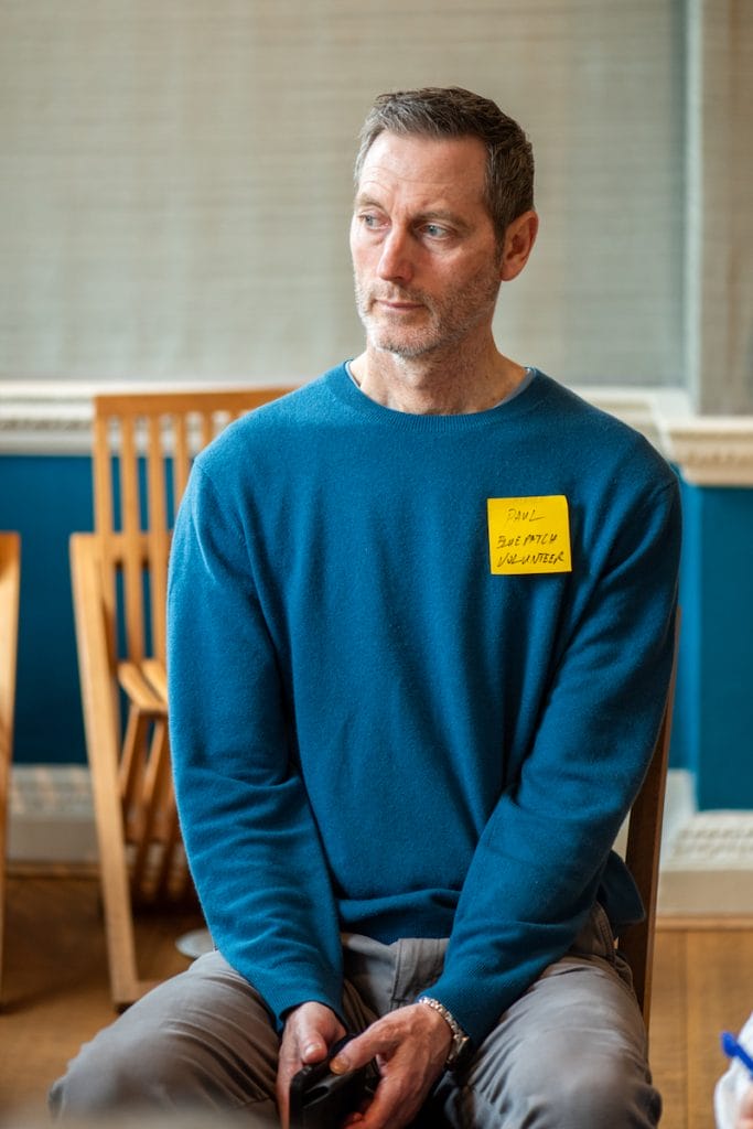 Paul, a Blue Patch volunteer, in a blue jumper, listening to a talk on cutting carbon emissions